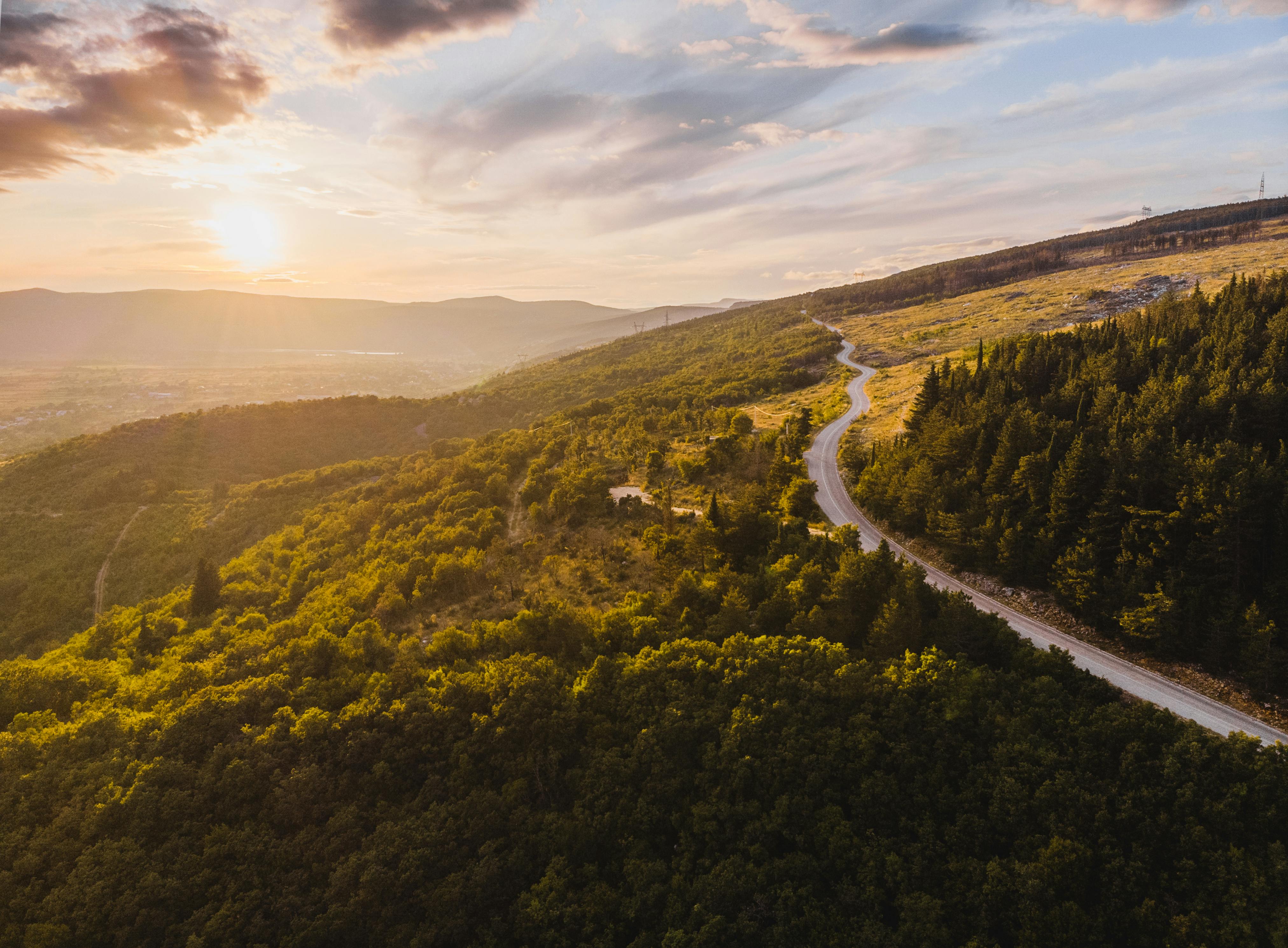 Una strada che si snoda al tramonto tra le colline boscose del Montenegro